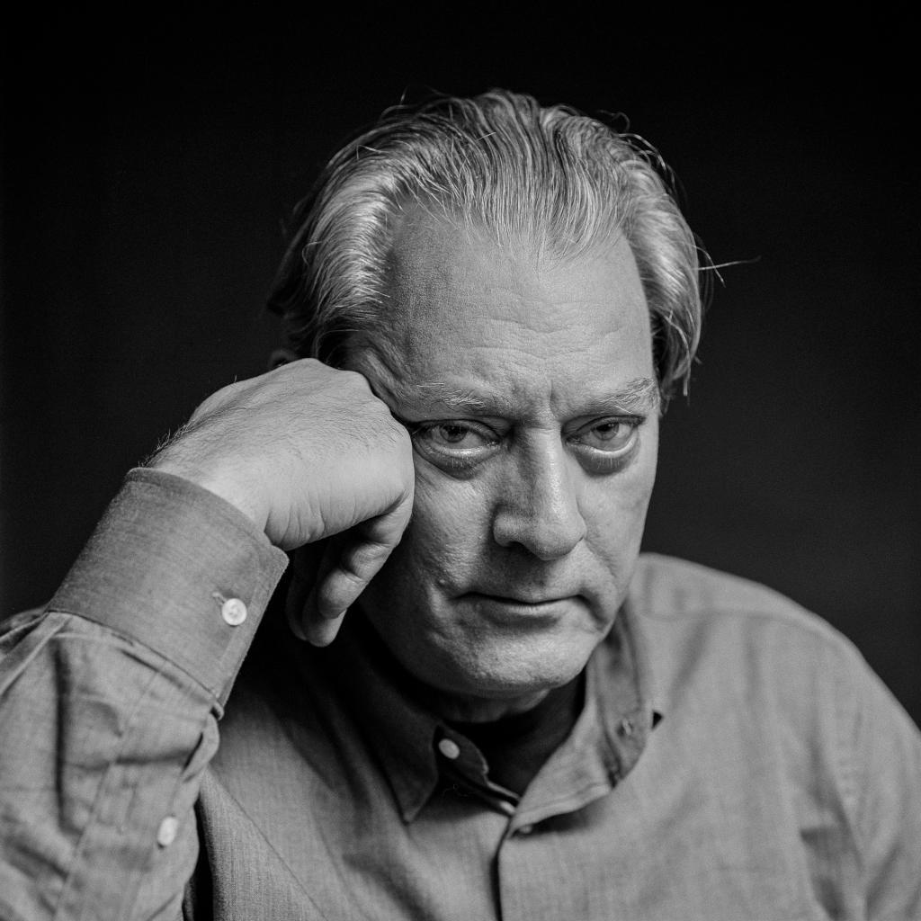 Paul Auster en blanco y negro, con expresión seria, apoyando la cabeza sobre los dedos, mirada directa a cámara.